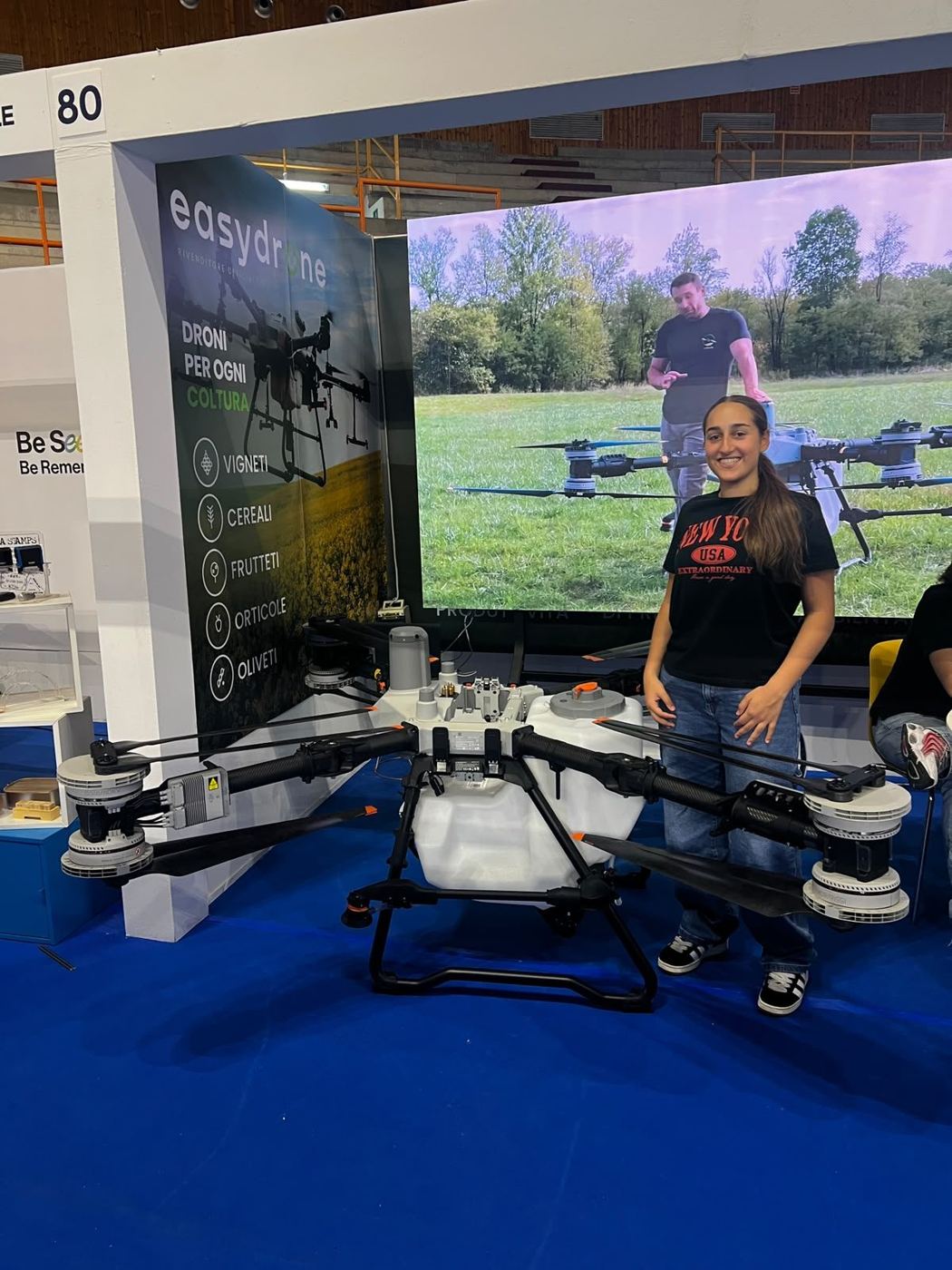 Una ragazza accanto a un drone agricolo esposto in fiera